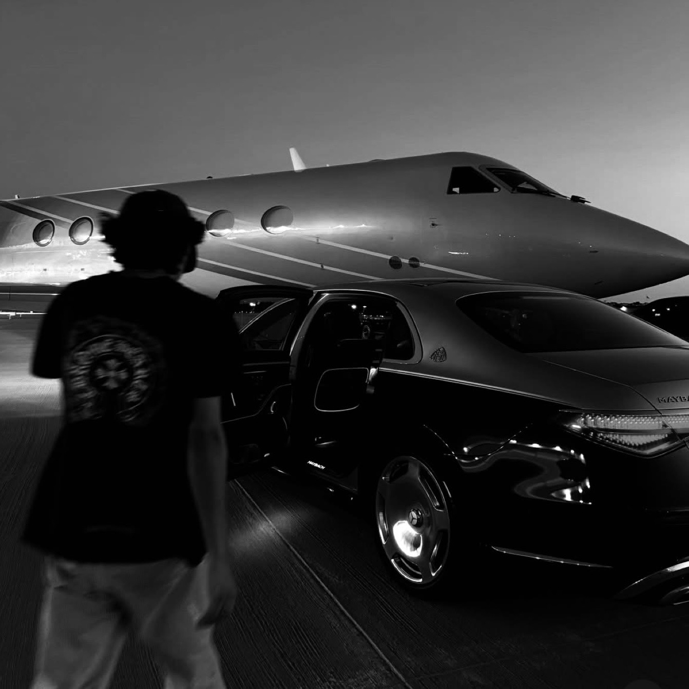 Man walking toward a private jet and luxury car at night